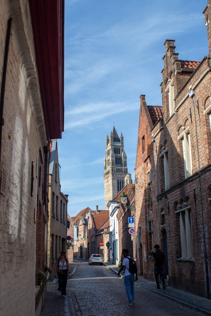 Cobblestone street in Brugge with historical architecture under clear blue sky.