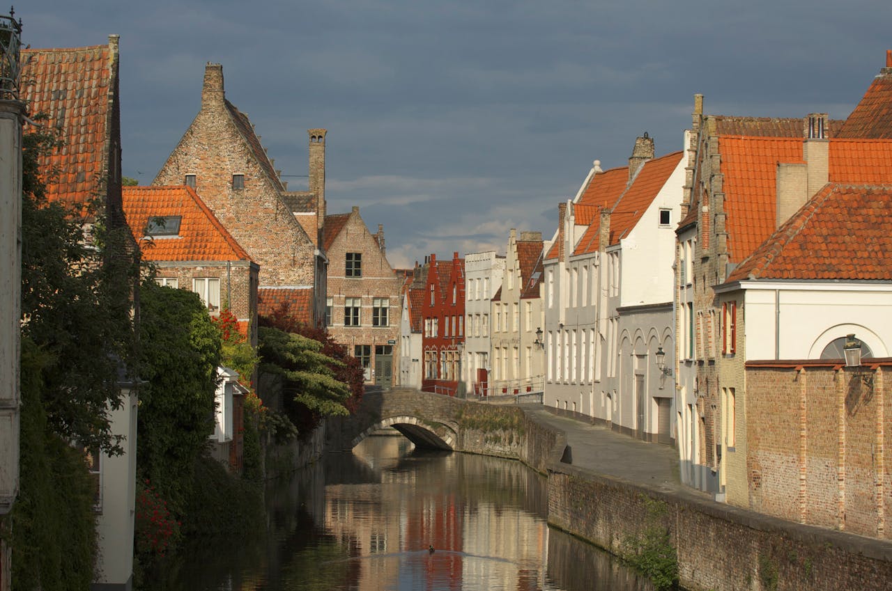 Charming canal scene with historic architecture in Bruges, Belgium, under a dramatic sky.