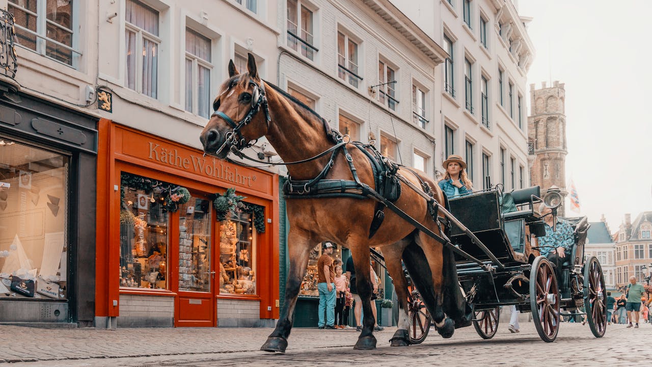 Classic horse-drawn carriage passing by shops in historic Bruges, Belgium.