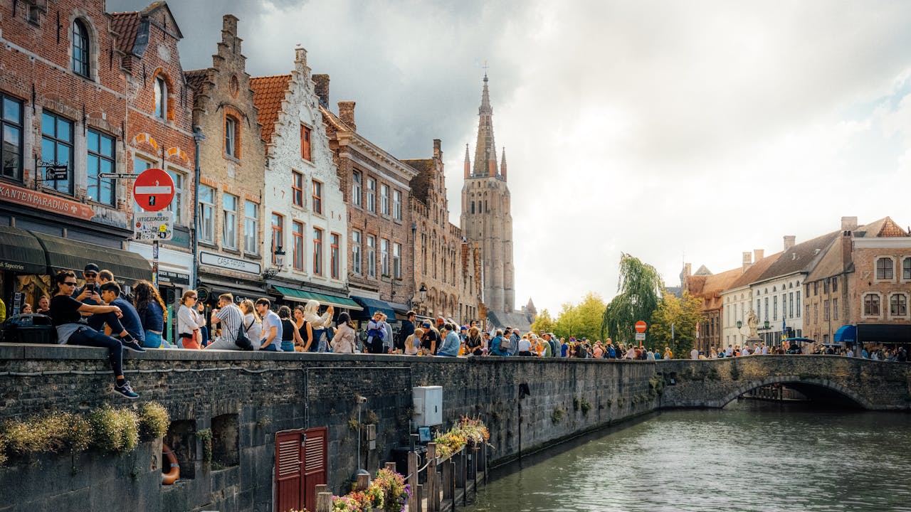 Picturesque scene of Bruges, showcasing historic buildings, a canal, and bustling crowds on a sunny day.